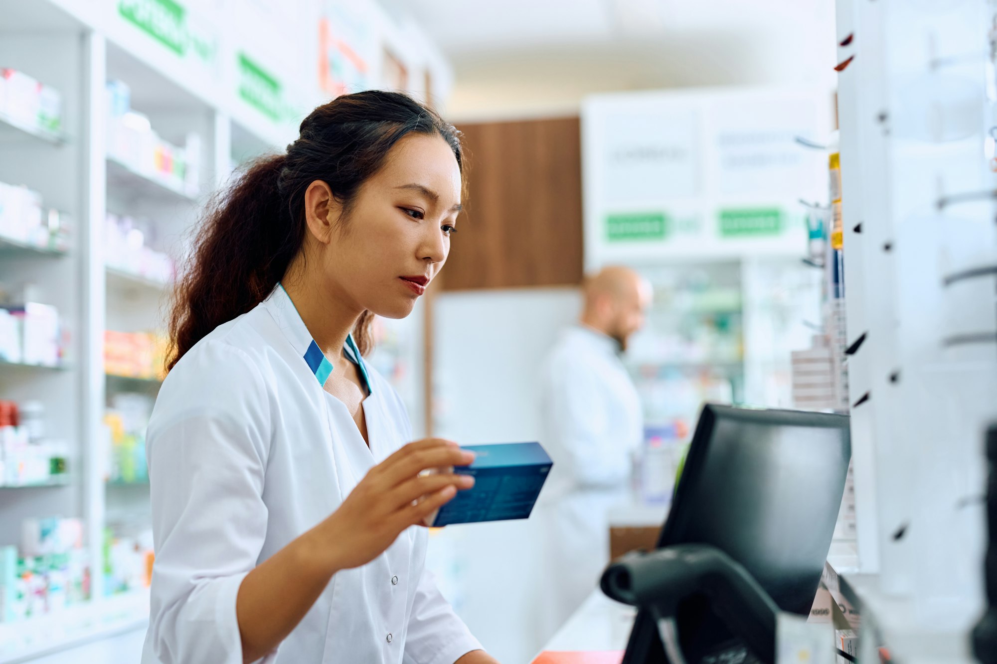 Chinese female pharmacist working on a computer in drugstore.